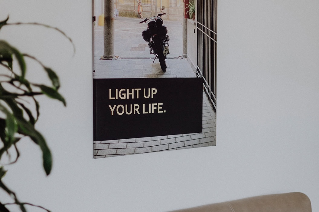 Ein Plakat mit einem Motorrad und dem Text LIGHT UP YOUR LIFE. hängt an einer weißen Wand.