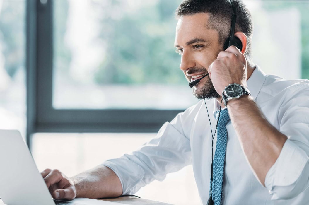 Lächelnder Mitarbeiter der Hotline für Erwachsene mit Laptop am Arbeitsplatz